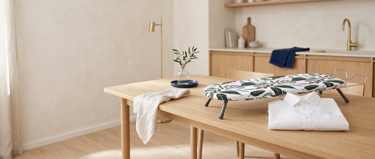 Tabletop ironing board on a light oak dining table with a folded shirt